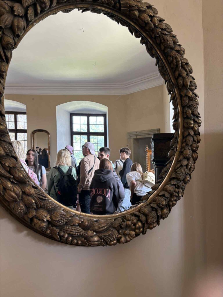 Zdjęcie lustra, w którym odbijają się uczestnicy wycieczki zwiedzający zamek